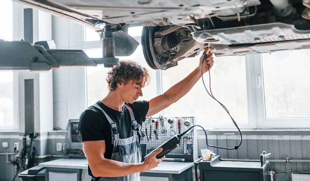 Kfz-Mechaniker überprüft Fahrzeug unter dem Auto in Werkstatt für Autoreparatur.